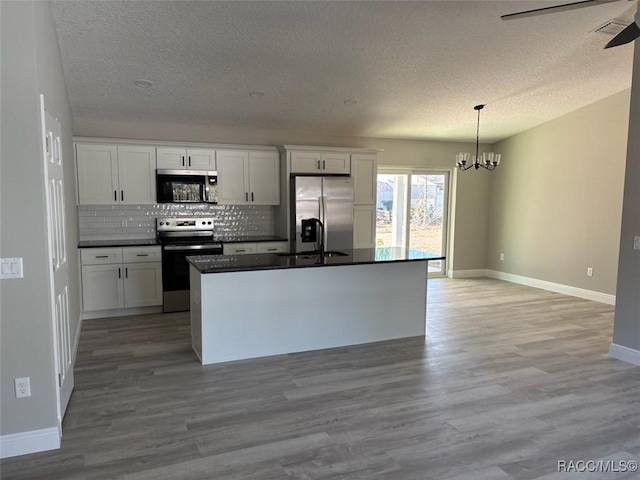 kitchen with dark countertops, white cabinetry, appliances with stainless steel finishes, light wood finished floors, and decorative backsplash