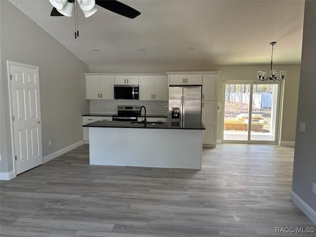 kitchen featuring a sink, stainless steel appliances, white cabinets, dark countertops, and ceiling fan with notable chandelier