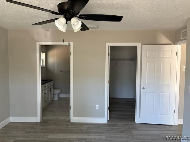 unfurnished bedroom with a closet, a spacious closet, baseboards, and wood finished floors