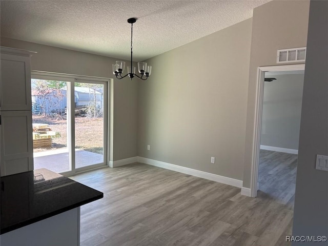 unfurnished dining area with an inviting chandelier, baseboards, visible vents, and light wood-type flooring