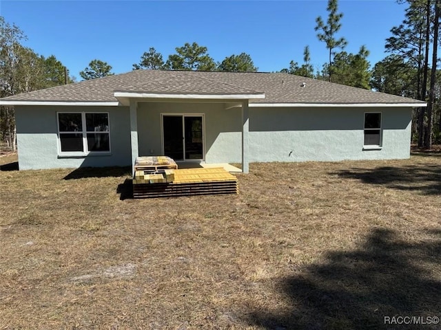 rear view of house featuring stucco siding, a lawn, and roof with shingles