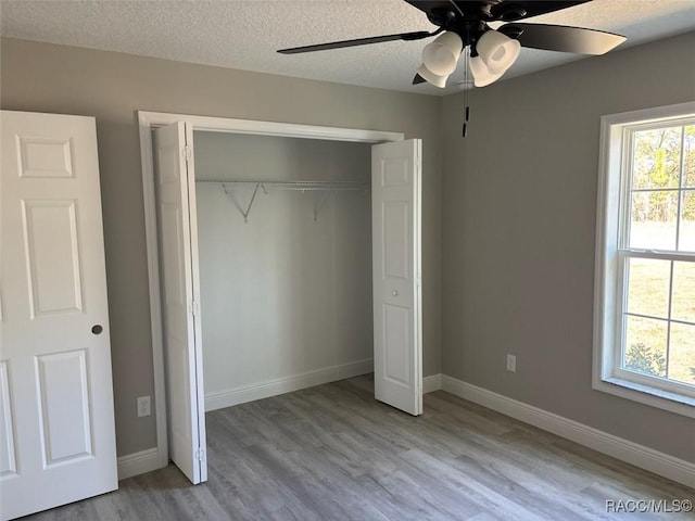 unfurnished bedroom with multiple windows, a textured ceiling, light wood-style flooring, and baseboards