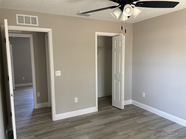 unfurnished bedroom featuring visible vents, baseboards, wood finished floors, a closet, and a textured ceiling