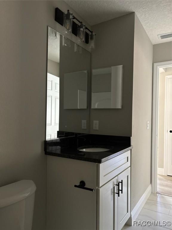 bathroom with vanity, toilet, visible vents, and a textured ceiling