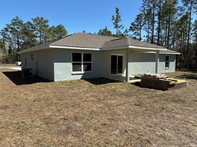 rear view of property with stucco siding, a shingled roof, a lawn, and central AC