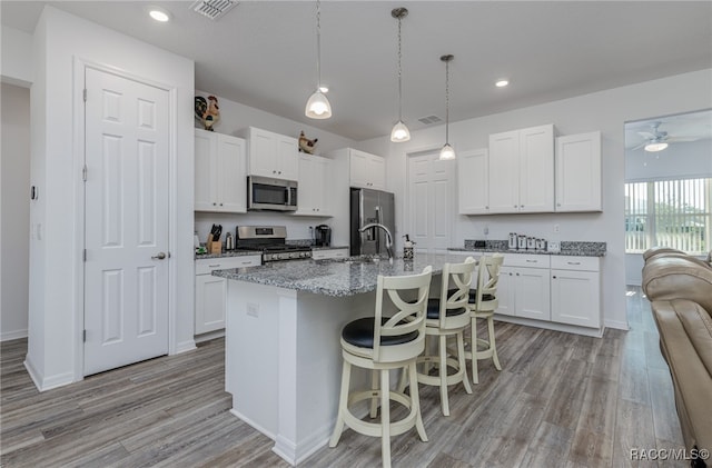 kitchen with ceiling fan, light wood-type flooring, an island with sink, appliances with stainless steel finishes, and white cabinetry