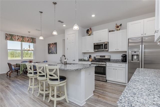 kitchen featuring light stone countertops, white cabinetry, stainless steel appliances, pendant lighting, and a center island with sink