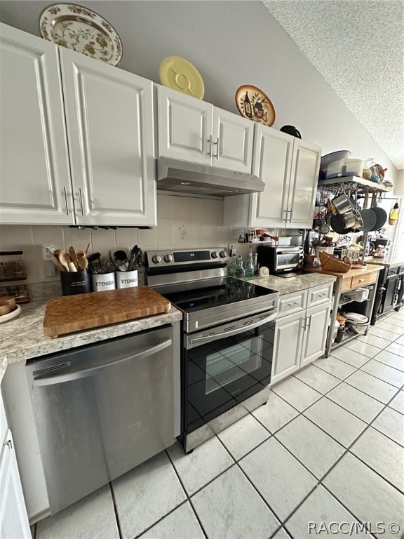 kitchen with appliances with stainless steel finishes, a textured ceiling, white cabinets, lofted ceiling, and light tile patterned flooring