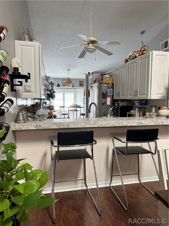 kitchen featuring a breakfast bar area, stainless steel fridge, a textured ceiling, and dark hardwood / wood-style floors