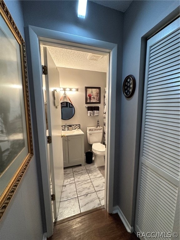 bathroom with vanity, toilet, wood-type flooring, and a textured ceiling