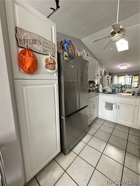 kitchen with white cabinets, stainless steel fridge, lofted ceiling, and light tile patterned floors