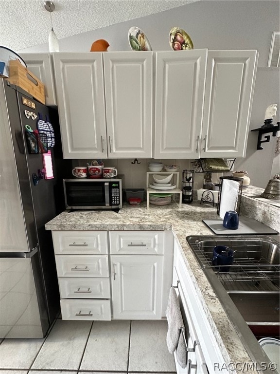 kitchen featuring lofted ceiling, white cabinets, stainless steel appliances, and a textured ceiling