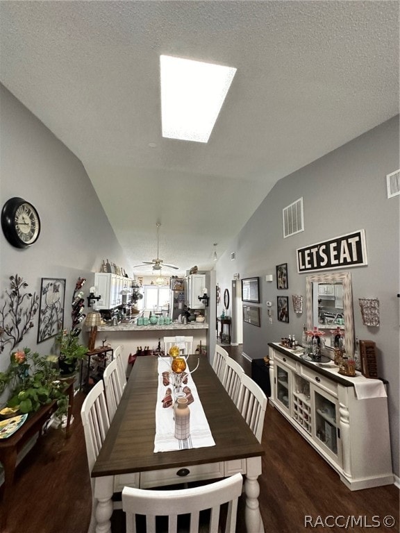 dining space featuring ceiling fan, dark hardwood / wood-style floors, lofted ceiling with skylight, and a textured ceiling