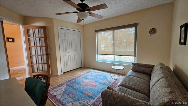 living room with ceiling fan, a textured ceiling, and light hardwood / wood-style flooring