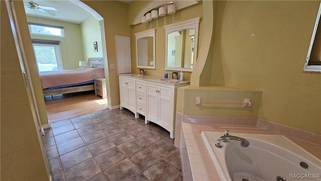 bathroom with tile patterned flooring, vanity, a relaxing tiled tub, and ceiling fan