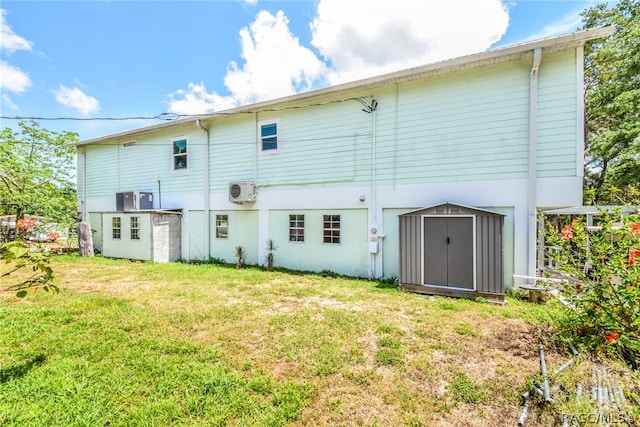 back of house with a storage shed, a yard, and ac unit