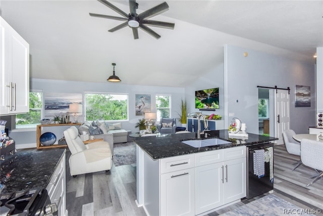 kitchen featuring vaulted ceiling, sink, a barn door, white cabinets, and an island with sink