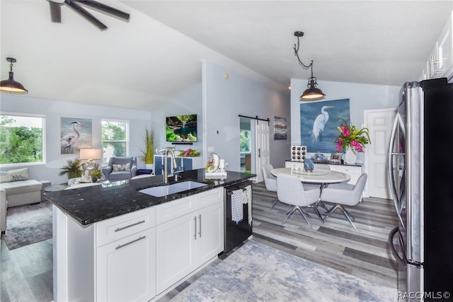 kitchen with dark stone counters, sink, a barn door, white cabinetry, and stainless steel refrigerator