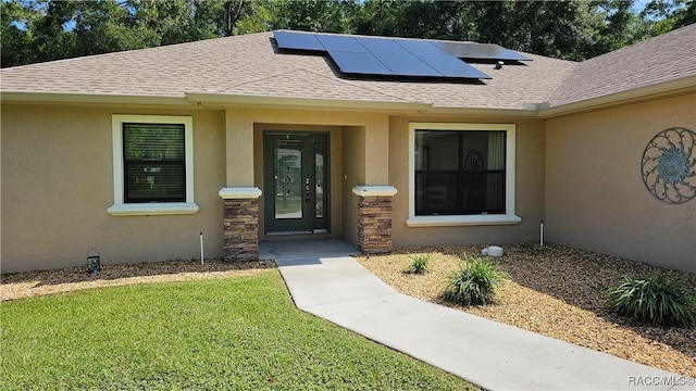 3153 N Chandler Dr, Hernando, FL 34442 - view of exterior entry with roof mounted solar panels, stucco siding, a shingled roof, and a lawn