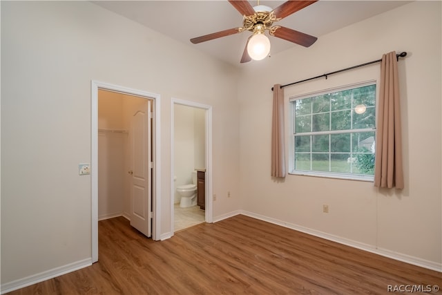 unfurnished bedroom with ensuite bath, hardwood / wood-style flooring, ceiling fan, a spacious closet, and a closet