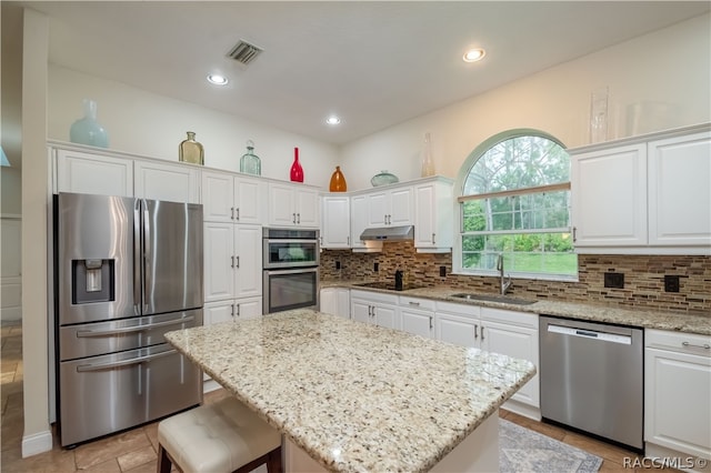 kitchen with light stone counters, stainless steel appliances, sink, a center island, and white cabinetry