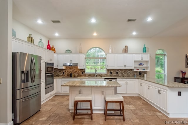 kitchen featuring kitchen peninsula, a kitchen breakfast bar, stainless steel appliances, sink, and a kitchen island