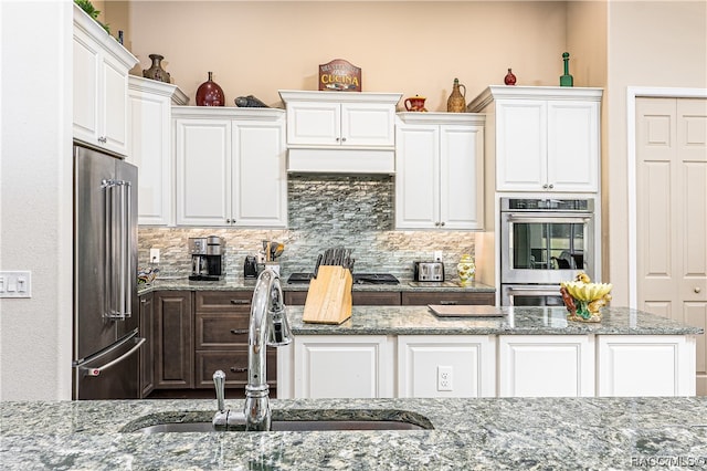 kitchen with decorative backsplash, light stone counters, stainless steel appliances, sink, and white cabinetry