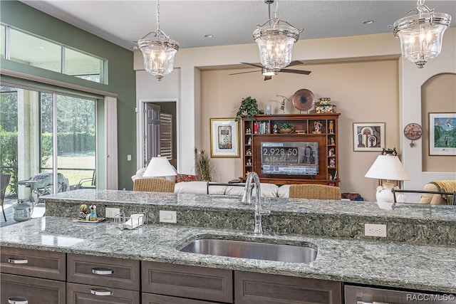 kitchen featuring light stone countertops, dark brown cabinetry, ceiling fan, and sink