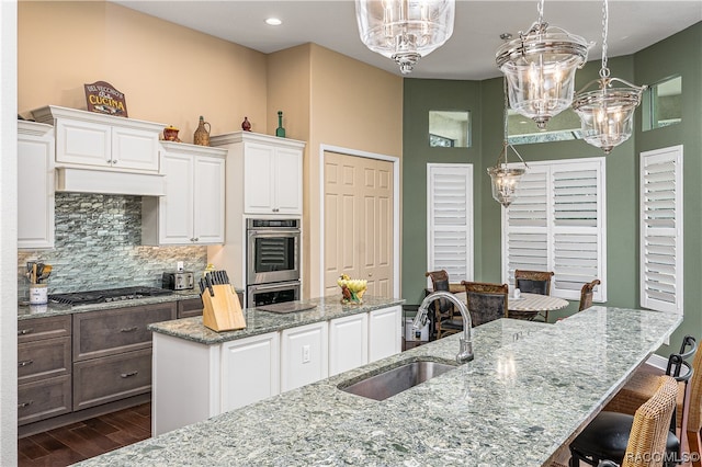 kitchen featuring pendant lighting, sink, light stone countertops, a large island, and white cabinetry