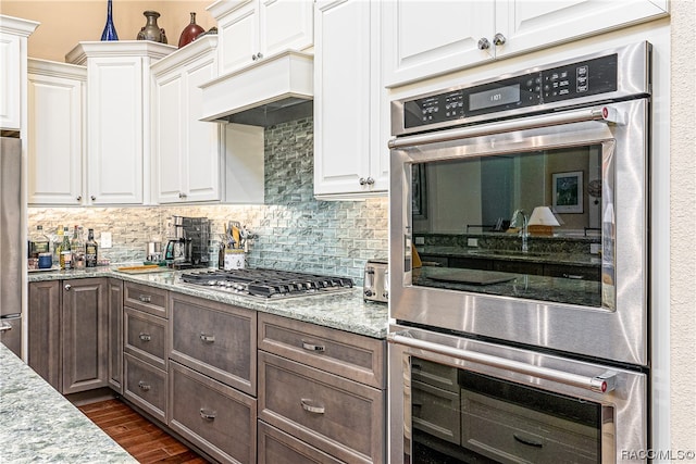 kitchen with light stone countertops, dark wood-type flooring, backsplash, white cabinets, and appliances with stainless steel finishes