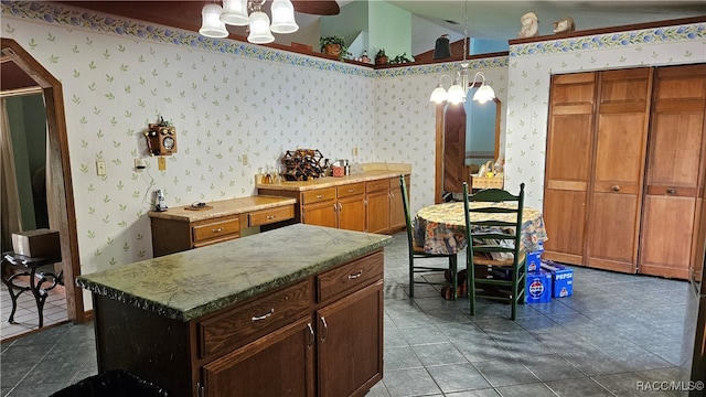 kitchen with ceiling fan with notable chandelier, vaulted ceiling, tile patterned flooring, decorative light fixtures, and a kitchen island