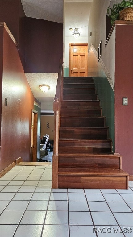 staircase featuring tile patterned flooring, a textured ceiling, and vaulted ceiling