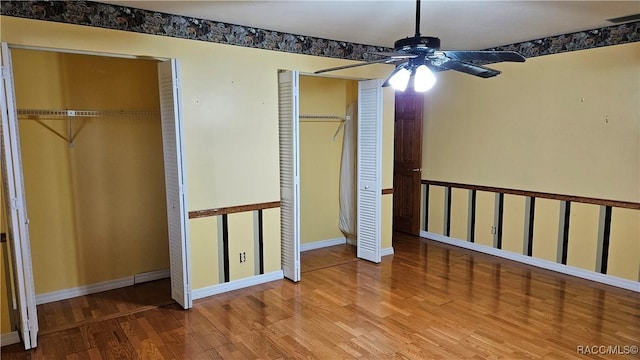 unfurnished bedroom with multiple closets, ceiling fan, and hardwood / wood-style floors