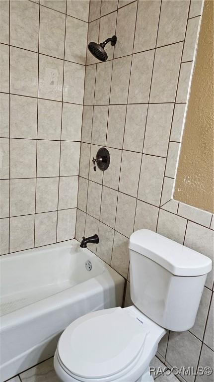 bathroom featuring tile walls, tiled shower / bath, and toilet