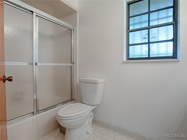 bathroom with tile patterned flooring, toilet, and bath / shower combo with glass door