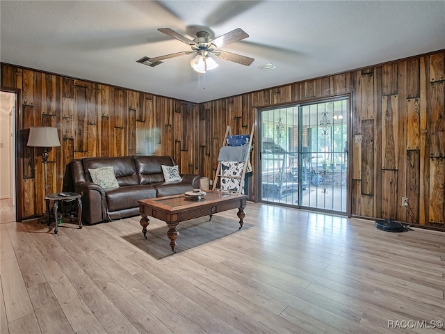 living room featuring light hardwood / wood-style flooring, ceiling fan, and wooden walls