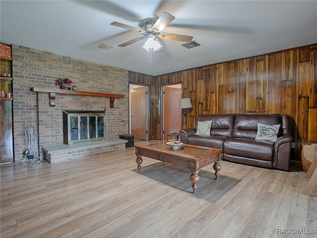 living room with wood walls, a brick fireplace, ceiling fan, a textured ceiling, and light hardwood / wood-style floors