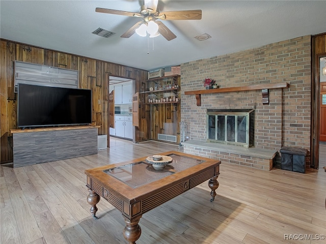 living room with ceiling fan, a brick fireplace, wood walls, light hardwood / wood-style floors, and a textured ceiling