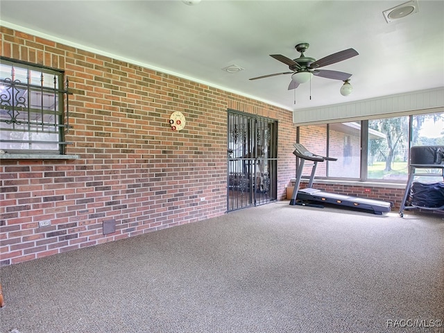 workout area with carpet flooring, ceiling fan, and brick wall