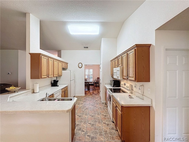 kitchen featuring lofted ceiling, white appliances, sink, a textured ceiling, and kitchen peninsula