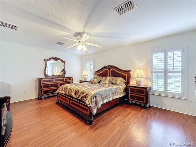 bedroom with multiple windows, ceiling fan, a textured ceiling, and hardwood / wood-style flooring