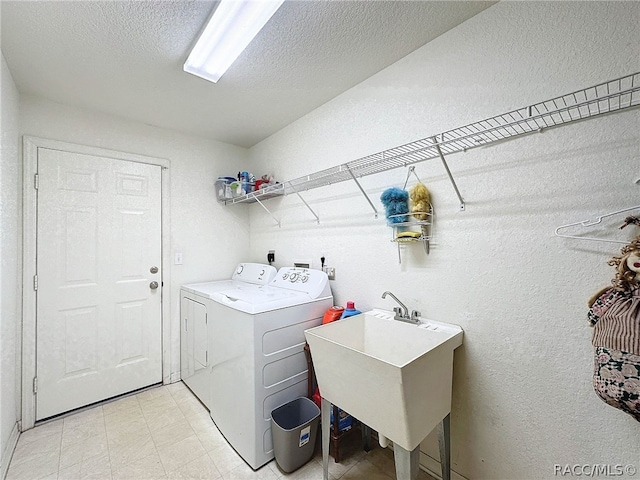 clothes washing area featuring washer and clothes dryer, a textured ceiling, and sink