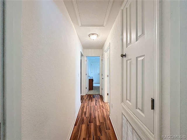 hall with wood-type flooring, a textured ceiling, and ornamental molding