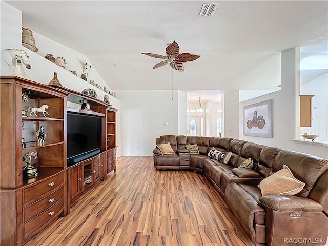 living room featuring ceiling fan with notable chandelier, light wood-type flooring, a textured ceiling, and lofted ceiling