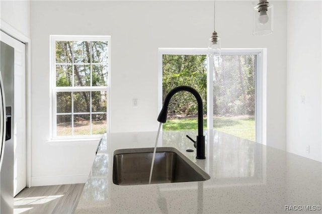 kitchen with a wealth of natural light, hanging light fixtures, light stone countertops, and a sink