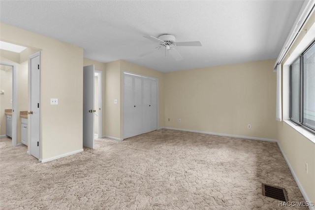 unfurnished bedroom with light carpet, ensuite bathroom, ceiling fan, a textured ceiling, and a closet