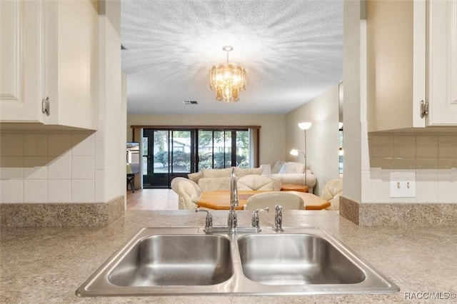 kitchen featuring decorative backsplash, sink, a notable chandelier, hardwood / wood-style floors, and white cabinetry