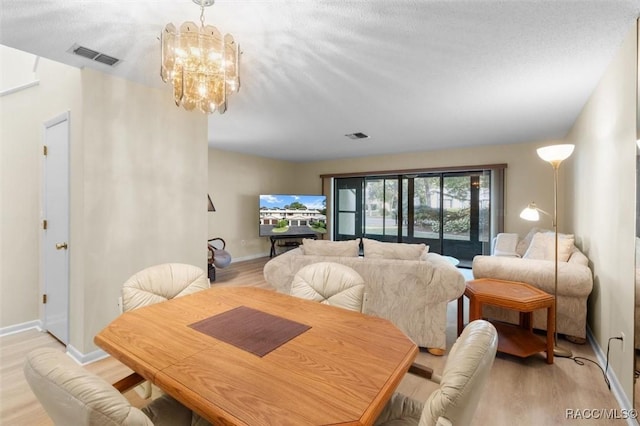 dining area with a textured ceiling, light hardwood / wood-style floors, and an inviting chandelier