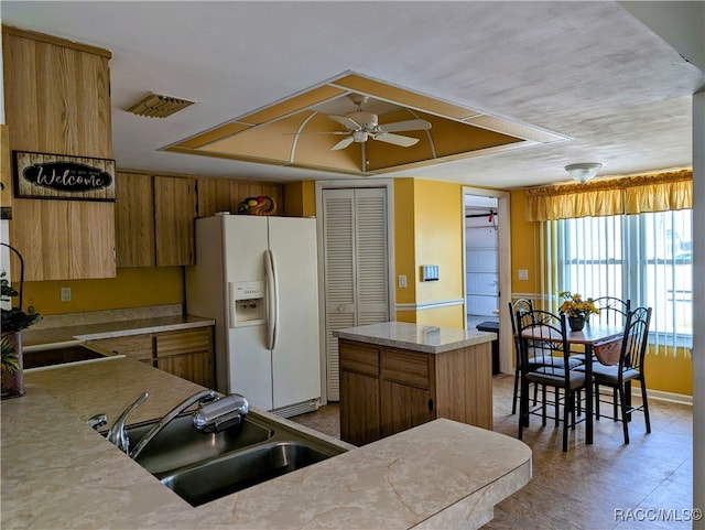 kitchen featuring white refrigerator with ice dispenser, a kitchen island, ceiling fan, and sink