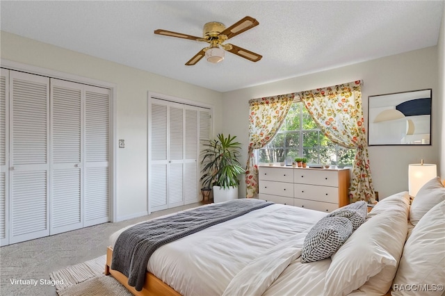 bedroom featuring light carpet, two closets, ceiling fan, and a textured ceiling